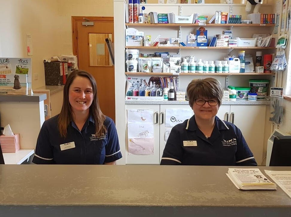 Two members of the Flett & Carmichael team smiling at the reception desk